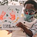 A black child holding a sign on the top of his dad's shoulders