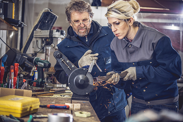 a tradeswoman grinding metal with her boss giving her instructions