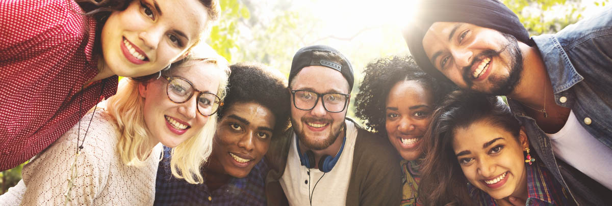 un groupe diversifié d’étudiants canadiens blottis autour d’une caméra et souriants