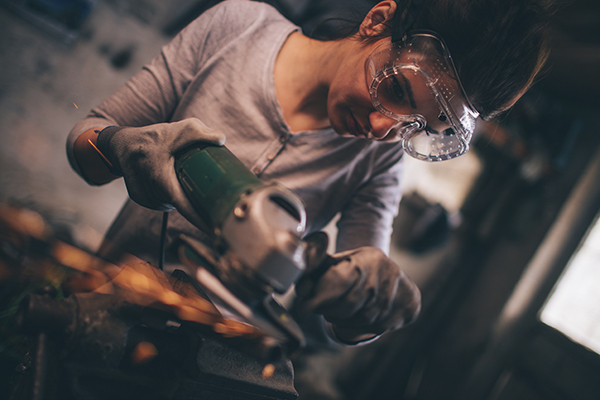 a skilled trades woman using a grinder and cutting a metal part